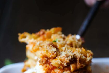 A spoonful of cheesy baked mostaccioli is served from a casserole dish.