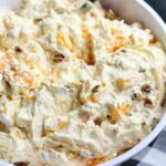 A close up image of bowl of orange cream fruit salad topped with chopped pecans.