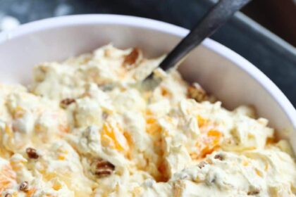 A close up image of bowl of orange cream fruit salad topped with chopped pecans.