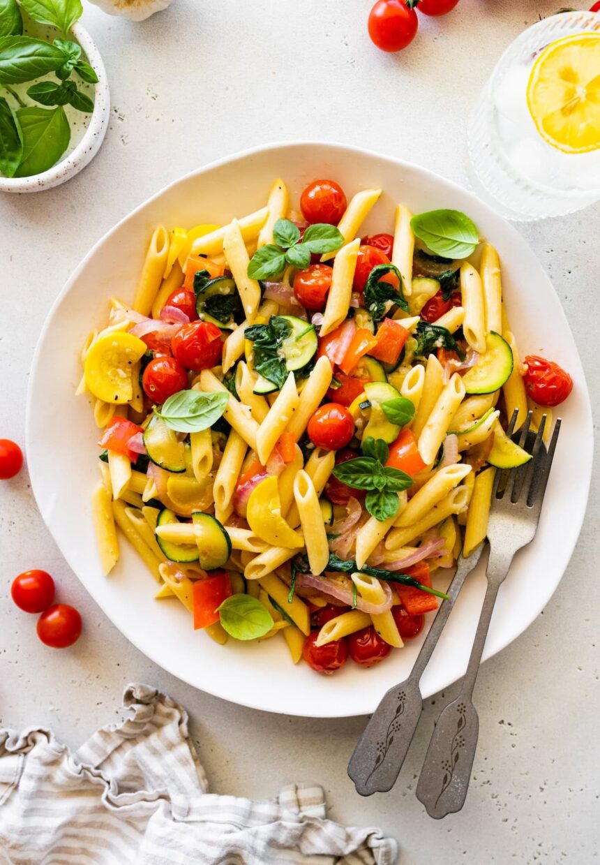 A serving of pasta primavera on a plate topped with fresh herbs.