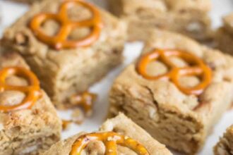 Peanut butter pretzel blondie squares each topped with a pretzel and a spoonful of peanut butter sitting on parchment paper