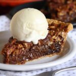 A slice of pecan pie on a white plate with a scoop of ice cream