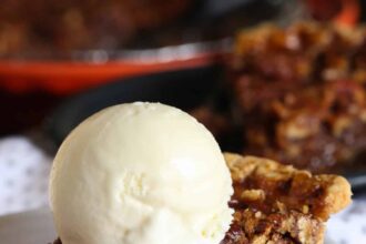 A slice of pecan pie on a white plate with a scoop of ice cream