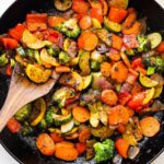 A cast iron skillet of sautéed vegetables including broccoli, carrots, onion, tomatoes, zucchini, and more.