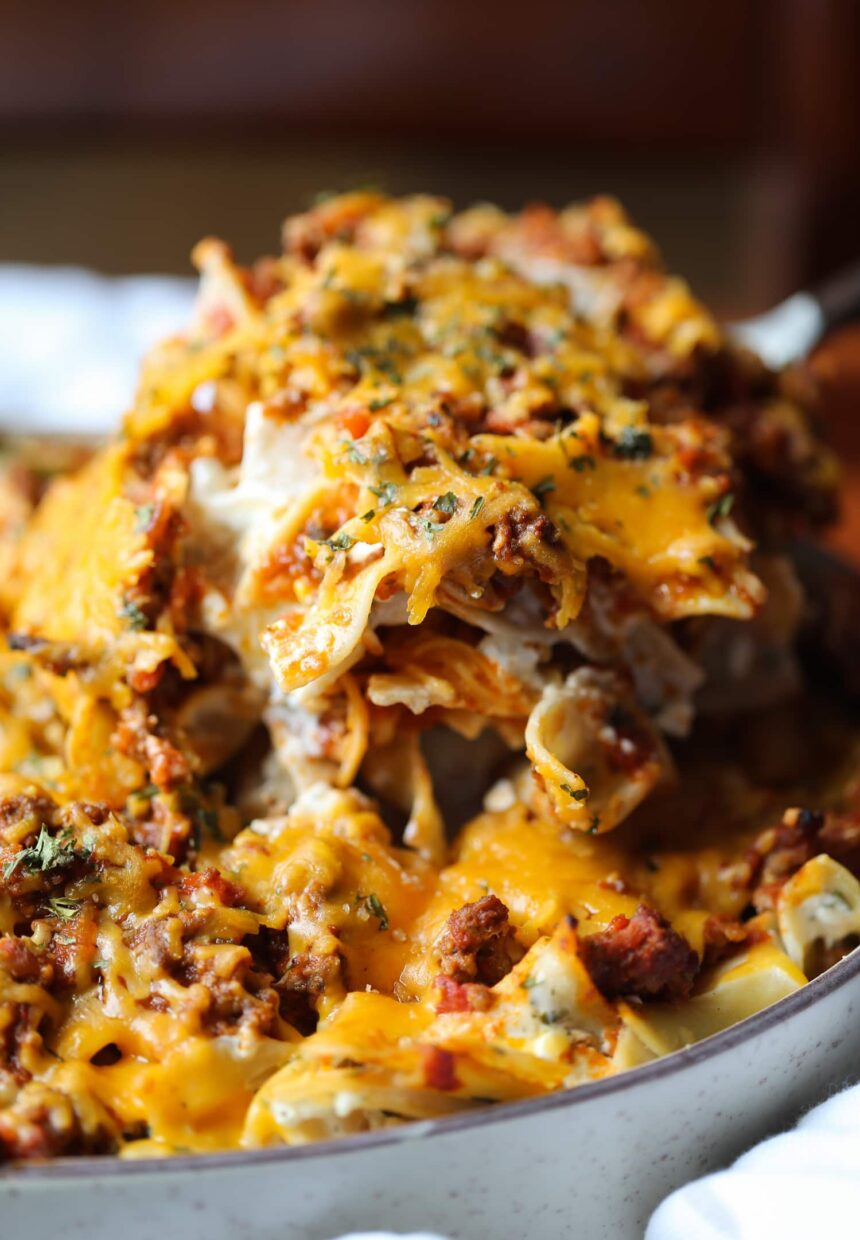 A scoop of noodle bake is lifted out of a casserole dish.