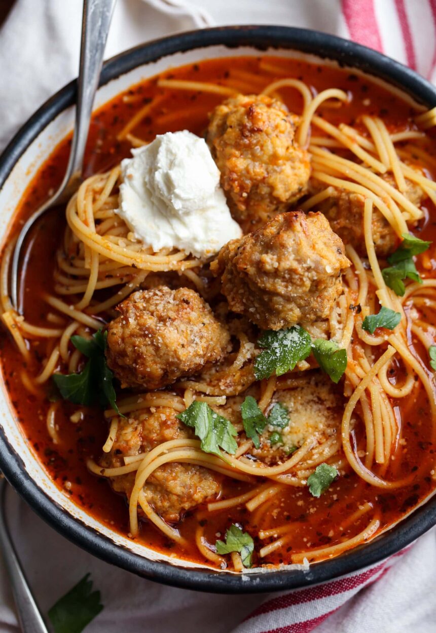 Bowl of spaghetti and meatball soup topped with parmesan cheese and ricotta