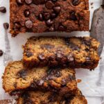 Three slices of vegan zucchini bread with chocolate chips leaning against one another near a loaf.