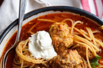 Bowl of spaghetti and meatball soup topped with parmesan cheese and ricotta