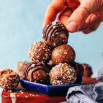 Picking up a seedy nut-free tahini snack bite from a stack with more bites