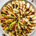 A large plate of apple nachos topped with a date caramel drizzle, mini chocolate chips, and pecans.