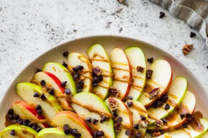 A large plate of apple nachos topped with a date caramel drizzle, mini chocolate chips, and pecans.