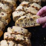 A hand taking a piece of biscotti from a serving tray