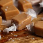 Homemade caramels wrapped in wax paper, arranged on a wood surface.