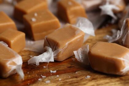 Homemade caramels wrapped in wax paper, arranged on a wood surface.