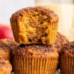 Two apple muffins stacked on one another with the top muffin having a large bite taken from it.