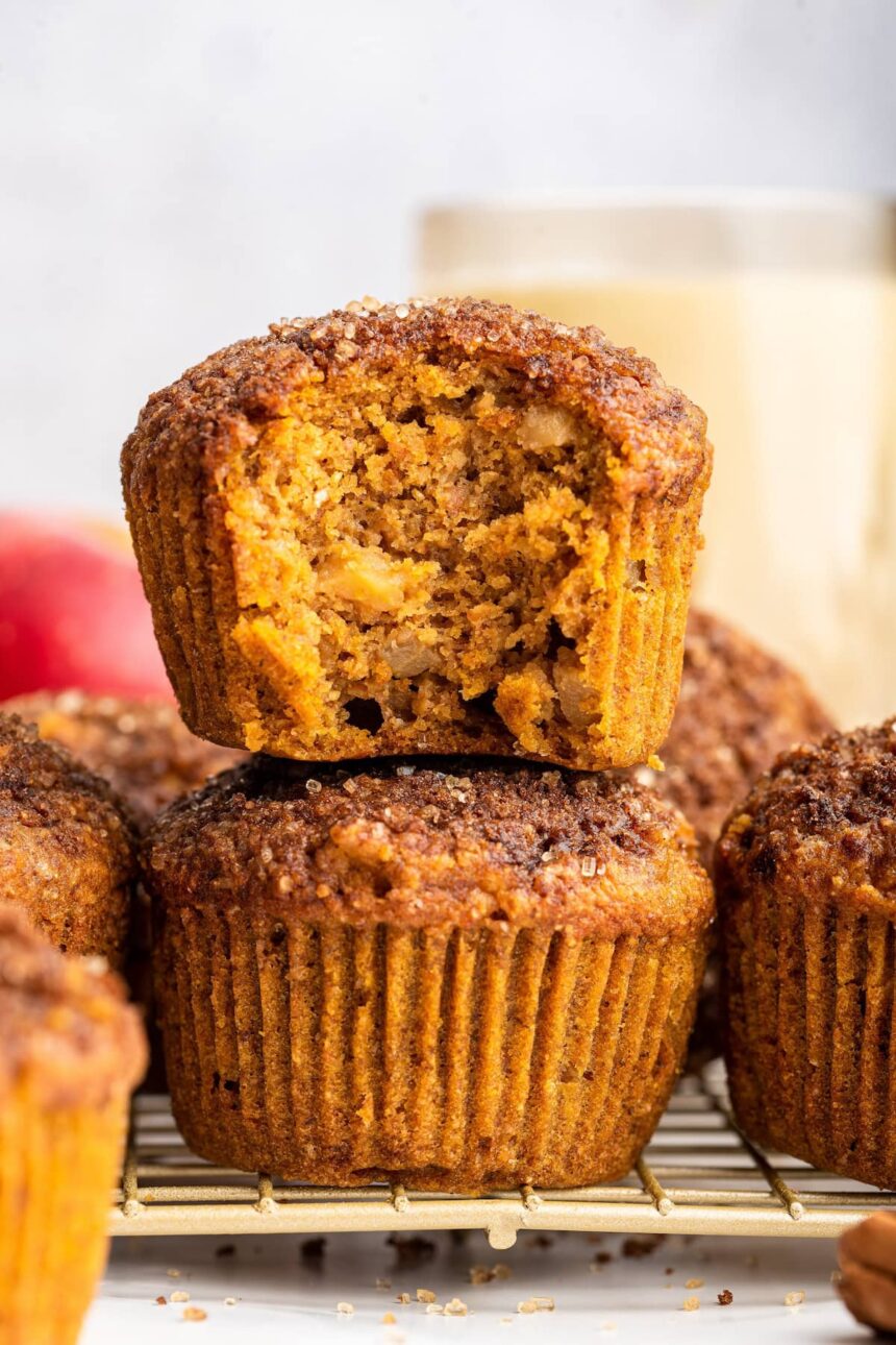 Two apple muffins stacked on one another with the top muffin having a large bite taken from it.