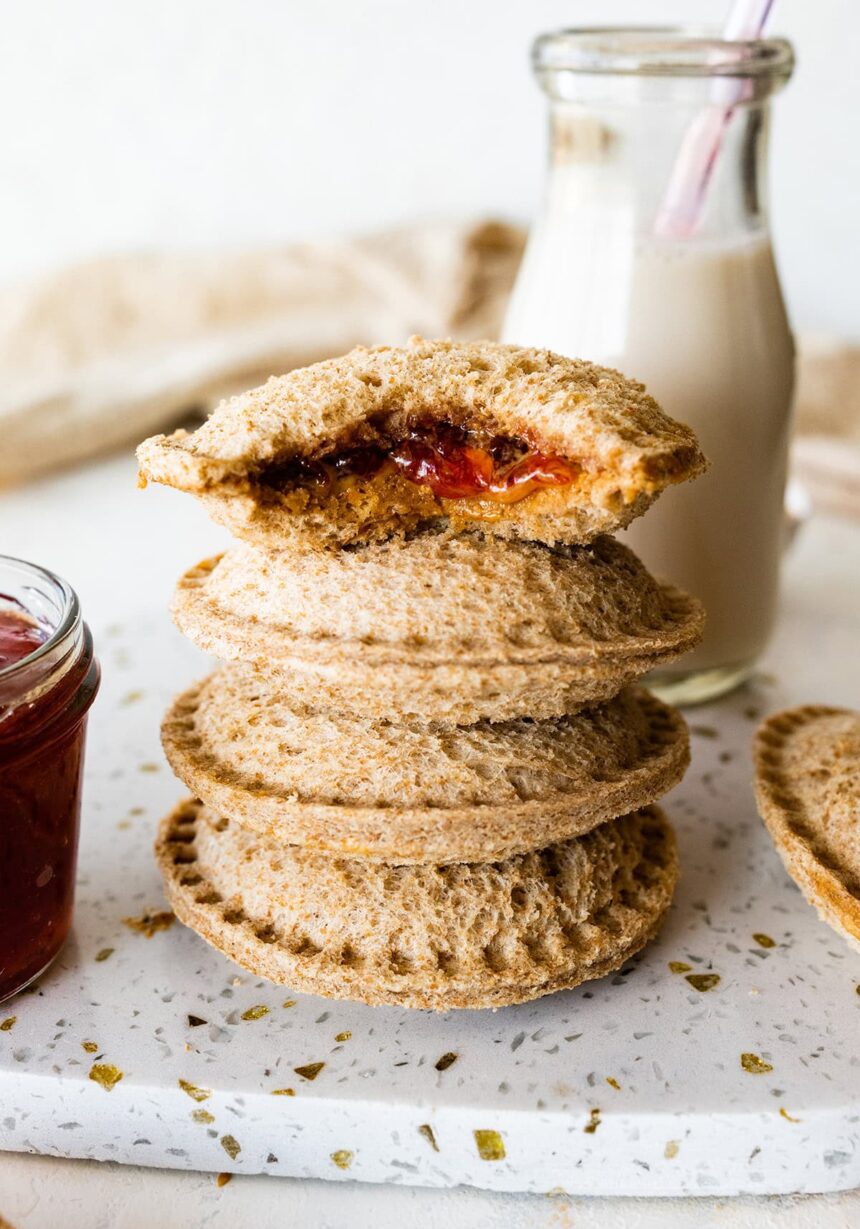 Four peanut butter uncrustables stacked on one another with the top having a bite taken from it.