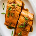 Two maple glazed salmon filets on a plate topped with green onion.