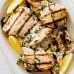 Multiple yogurt marinated chicken thighs on a plate with lemon wedges on the side.