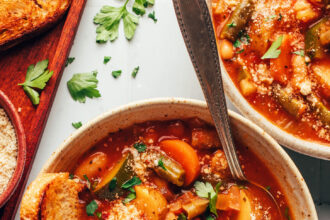 Bowls of veggie white bean minestrone topped with vegan parmesan cheese and parsley and served with toasted bread