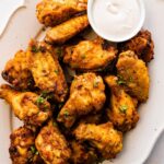 A large plate of air fried chicken wings topped with fresh herbs with a side of ranch.