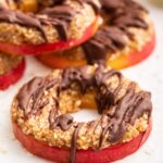 Multiple apple samoas near one another. The slices are topped with a chocolate drizzle.