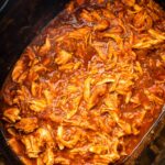 A slow cooker pot full of bbq shredded chicken.