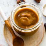 A glass jar of date caramel near a wooden spoon.