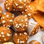 Multiple pumpkin muffins near one another with some stacked on top of others.