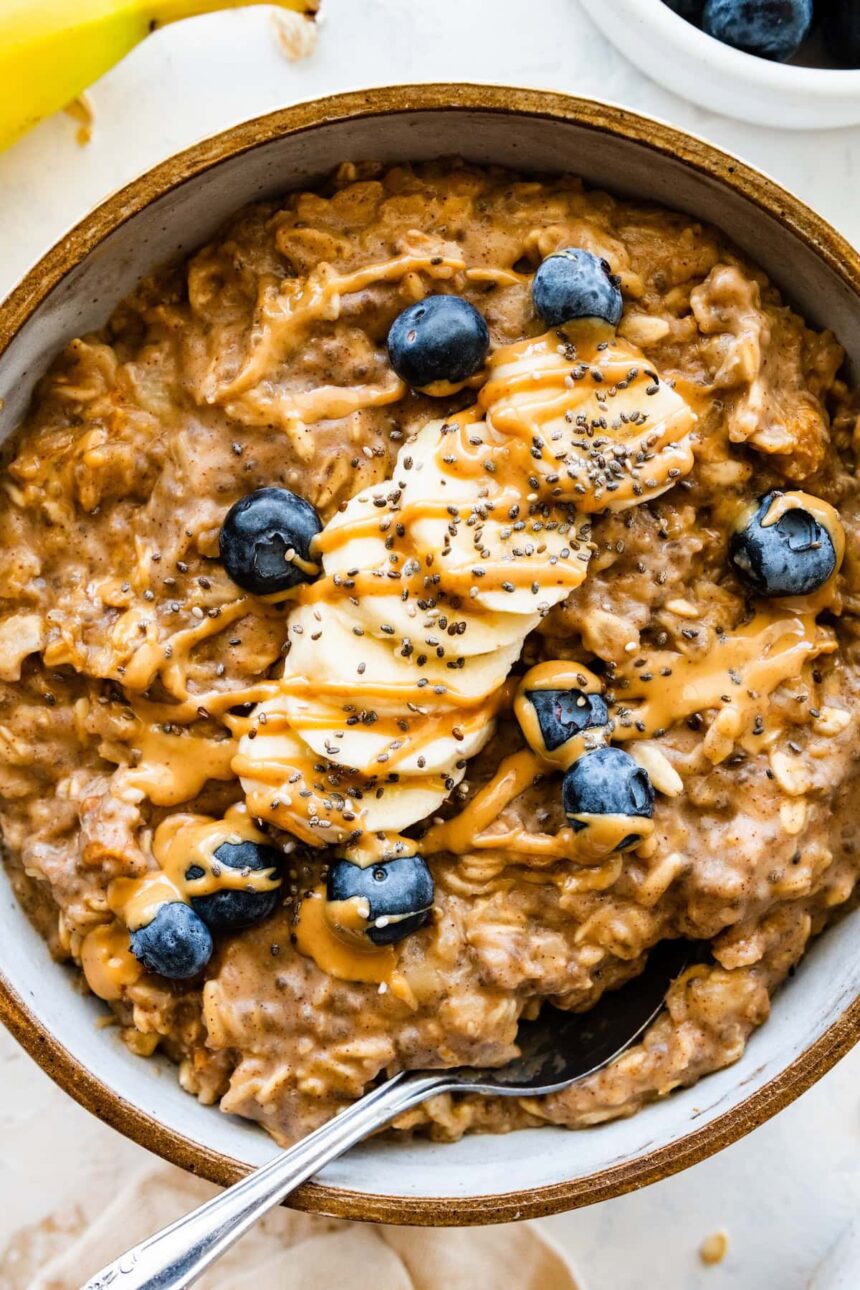 A bowl of peanut butter oatmeal topped with fresh banana slices, blueberries, a drizzle of peanut butter and chia seeds.