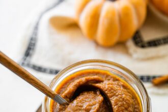 A glass jar full of pumpkin butter with a spoon inside.