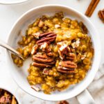 A bowl of pumpkin oatmeal with milk, and topped with pecans.