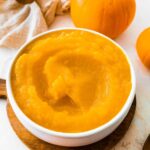 A homemade pumpkin puree in a bowl on a circular wooden board.