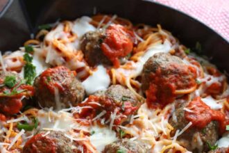 Spaghetti and Meatballs baked in a skillet topped with cheese and fresh parsley