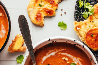 Bowls of spicy pumpkin tomato soup topped with coconut milk, cashews, cilantro, and naan