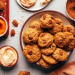 Bowl of fluffy pumpkin oat cookies next to a plate of frosted cookies and ingredients used to make the cookies