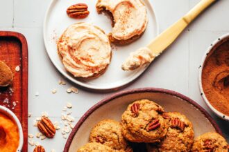 Bowl of fluffy pumpkin oat cookies next to a plate of frosted cookies and ingredients used to make the cookies