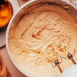 Using an electric mixer in a bowl of vegan pumpkin spice frosting