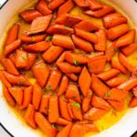 Glazed carrots cooked in a large pot and topped with fresh thyme.