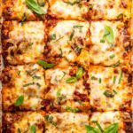 Healthy lasagna in a baking dish, cut into squares, and garnished with fresh basil and parsley.