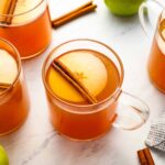 a glass of apple cider topped with an apple slice and a cinnamon stick.