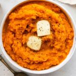 Mashed sweet potato in a bowl topped with two slices of butter and seasonings.