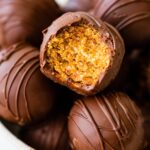 Chocolate covered peanut butter balls in a bowl with one ball having a bite taken from it.