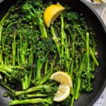 A pan of sautéed broccolini with lemon wedges and red pepper flakes.