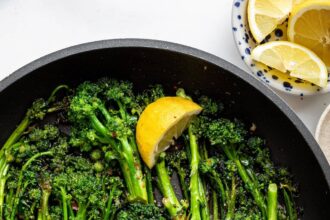 A pan of saut&eacute;ed broccolini with lemon wedges and red pepper flakes.