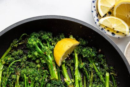 A pan of saut&eacute;ed broccolini with lemon wedges and red pepper flakes.