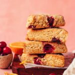 Stack of vegan gluten-free cranberry orange scones next to orange slices and cranberries