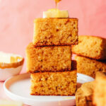 Drizzling honey onto a stack of gluten-free cornbread slices topped with butter