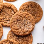 Multiple molasses cookies sprinkled with cane sugar with a glass of milk in the background.