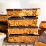 Four peanut butter bars stacked on top of each other on a wire cooling rack. The top bar has a bite taken out of it.